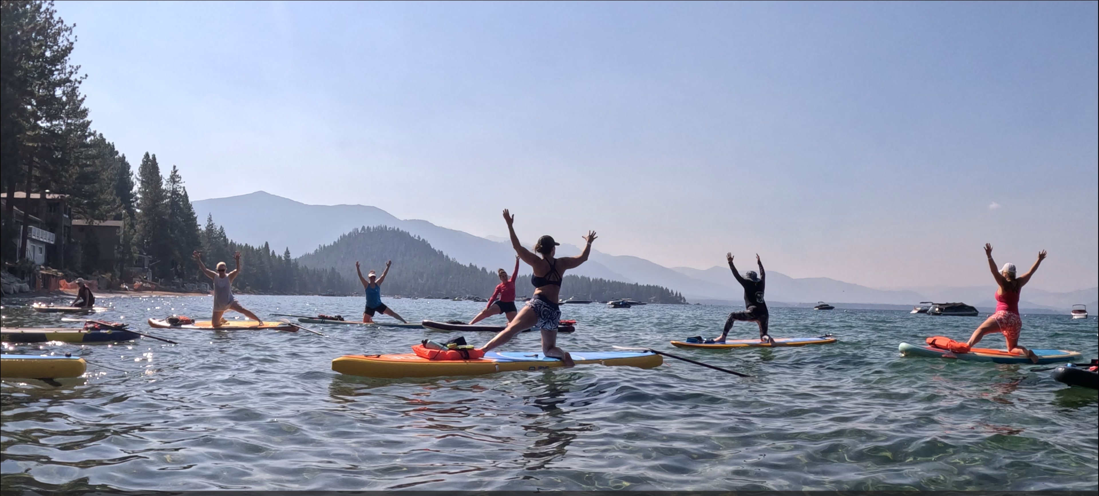 A woman seated in lotus on a paddleboard on a glassy alpine lake, Mt. Shasta rising through the pines.
